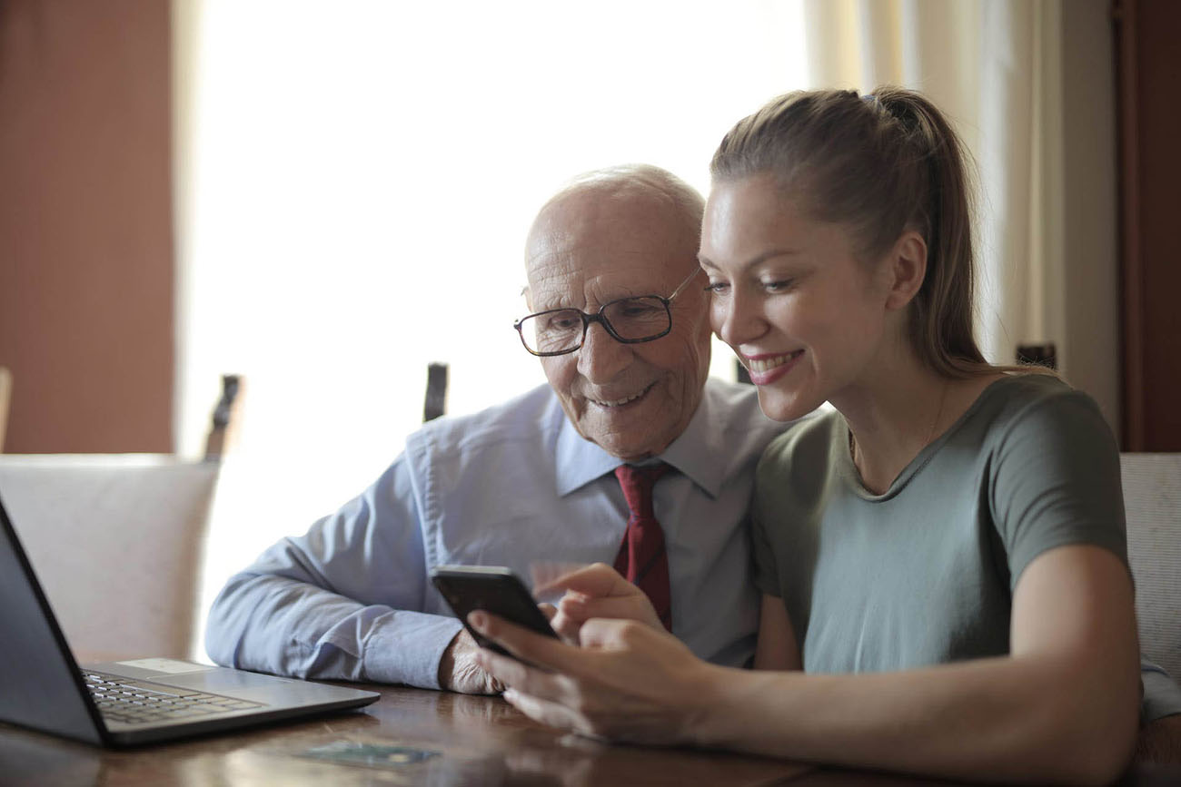 Ung dame og gammel mann som ser på skjermen til en mobiltelefon